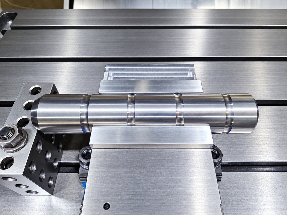 A turned and grooved shaft set up on a machine table with parallels and a vise